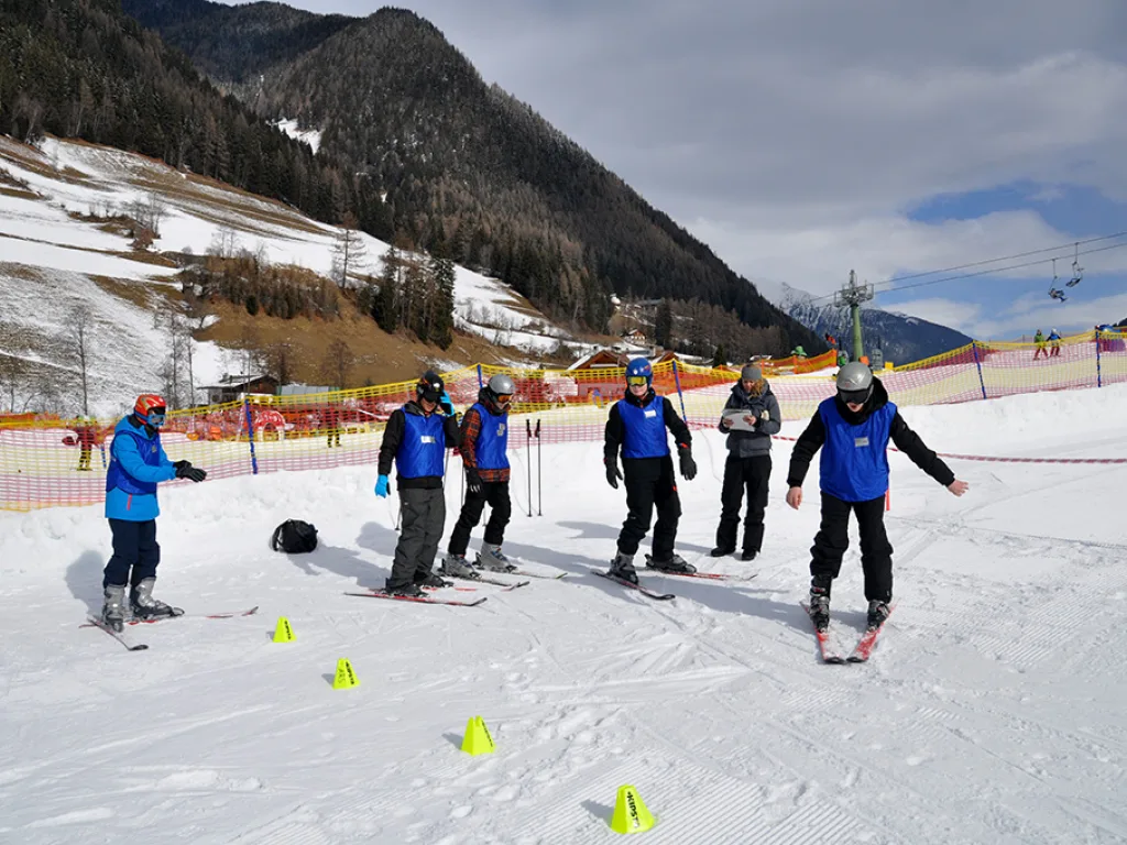 Skilehrkraft steht mit einer kleinen Gruppe auf dem Hang.